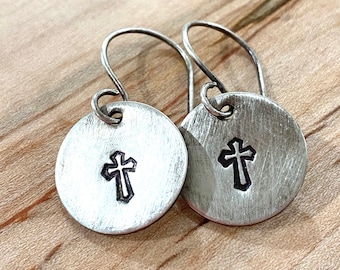 May include: Silver earrings with a small cross design on each round disc. The earrings have a simple, minimalist style.