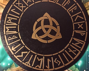 May include: A black circular wooden board with a gold triquetra symbol in the center. The board is surrounded by a ring of gold runes.