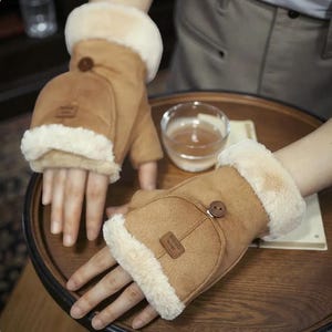 Puede incluir: Guantes sin dedos marrones con exterior de ante beige y ribete cremoso y esponjoso. Los guantes tienen cierre de botón y un pequeño parche rectangular. Diseñados para mantener las manos calientes dejando los dedos libres.