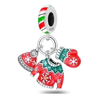 May include: A silver charm with a red, green, and white striped top. The charm has a ring with three dangling Christmas-themed pendants: a red sweater, a red hat, and a red mitten, all with white snowflake designs.