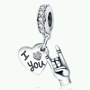 May include: A silver charm with a heart pendant that says "I you" and a hand gesture. The charm has a ring of clear stones and is marked S925.