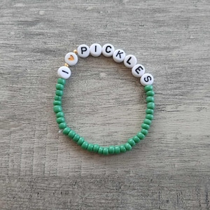 May include: Green beaded bracelet with white beads that spell out "I love pickles".