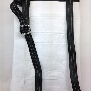 May include: White leather crossbody bag with black leather straps and stitching. The bag has a flap closure and a single compartment.