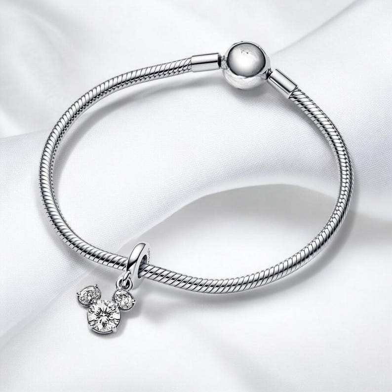 May include: A silver charm bracelet with a Mickey Mouse charm featuring clear cubic zirconia stones.