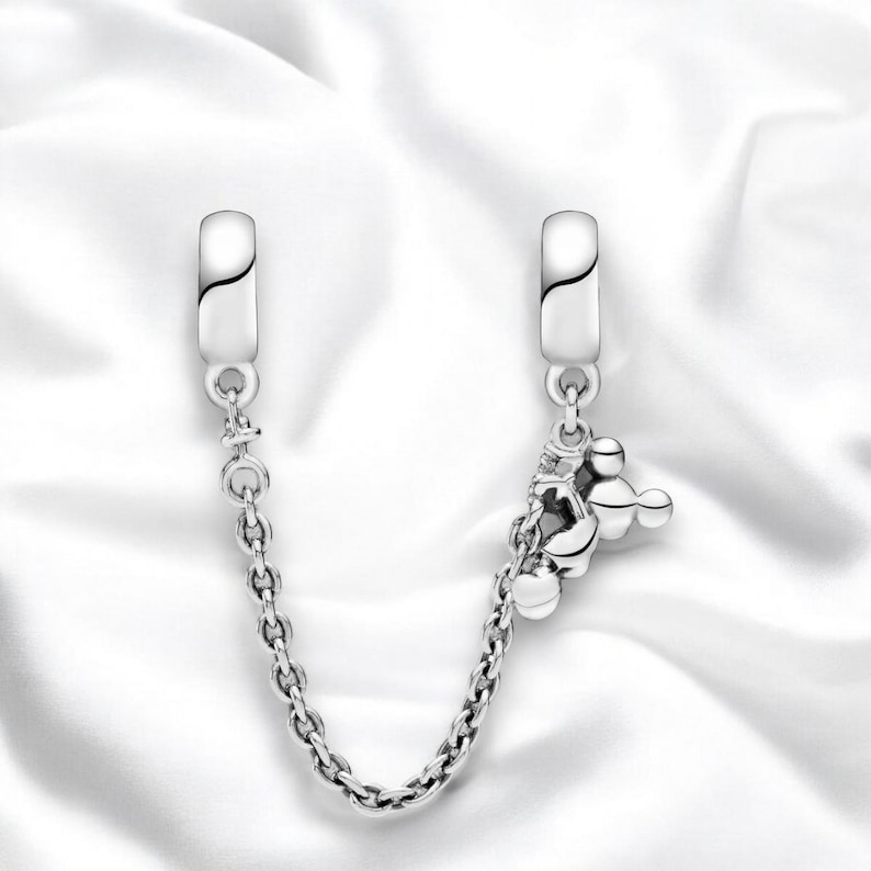 May include: Silver charm bracelet with a Mickey Mouse charm and a chain connector. The charm is made of silver and features a Mickey Mouse head with three round balls.