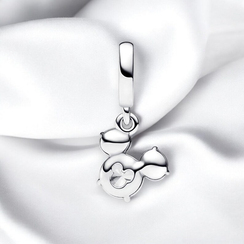 May include: Silver charm featuring a Mickey Mouse silhouette with a clear crystal in the center. The charm is designed to be attached to a bracelet or necklace.