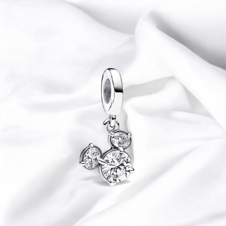 May include: A silver charm with a Mickey Mouse design featuring three clear cubic zirconia stones.