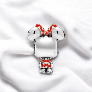 Pu&ograve; includere: Ciondolo in argento con un personaggio dei cartoni animati con grandi orecchie, un fiocco rosso con pois bianchi e un vestito rosso con pois bianchi.