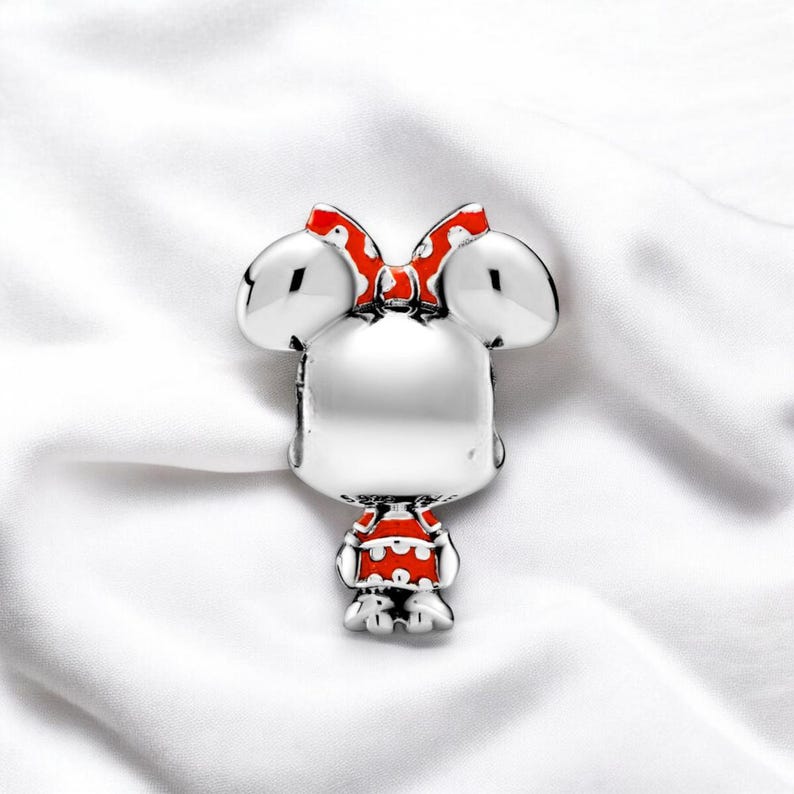 Pu&ograve; includere: Ciondolo in argento con un personaggio dei cartoni animati con grandi orecchie, un fiocco rosso con pois bianchi e un vestito rosso con pois bianchi.