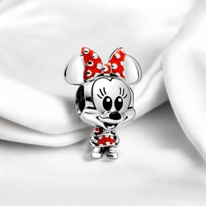 Pu&ograve; includere: Ciondolo in argento con una Minnie Mouse dei cartoni animati con un fiocco e un vestito a pois rossi e bianchi.