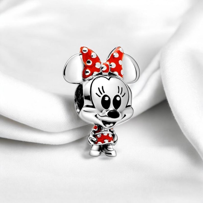 Pu&ograve; includere: Ciondolo in argento con una Minnie Mouse dei cartoni animati con un fiocco e un vestito a pois rossi e bianchi.