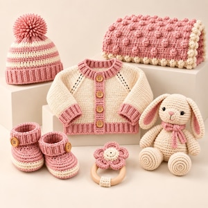 Può includere: Un set all'uncinetto composto da un berretto a righe rosa e crema con pon-pon, un cardigan crema con bordi rosa e quattro bottoni in legno, una coperta rosa e crema con texture a bolle, due scarpine, un sonaglio a fiore e un coniglietto crema.