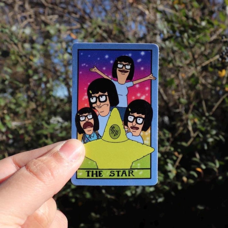 May include: A blue tarot card featuring a cartoon family with the text "THE STAR" at the bottom. The card has a yellow star in the center and a colorful background.