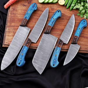 May include: A set of six kitchen knives with patterned steel blades and blue wooden handles. The handles have a dark brown accent and are secured with small rivets. The knives are arranged on a wooden cutting board.