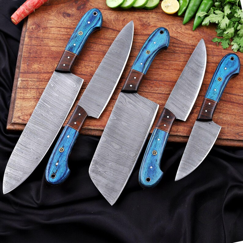 May include: A set of six kitchen knives with patterned steel blades and blue wooden handles. The handles have a dark brown accent and are secured with small rivets. The knives are arranged on a wooden cutting board.