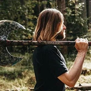May include: A person holding a large double-headed axe with a black leather handle and a silver blade. The axe has a decorative pattern on the blade.