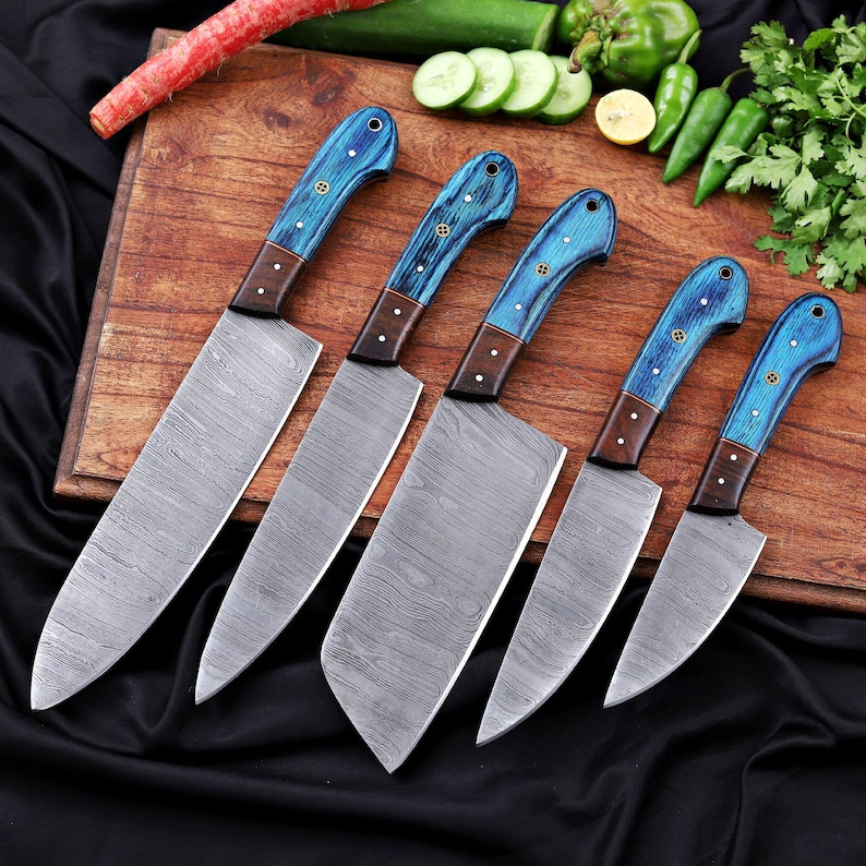 May include: A set of six kitchen knives with patterned steel blades and blue wooden handles. The handles have a dark brown bolster and are secured with small brass rivets. The knives are arranged on a wooden cutting board.