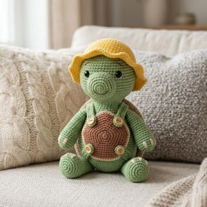 May include: A crocheted turtle plush toy featuring a light green body, a brown shell, and a yellow sun hat. The turtle wears green overalls with four small wooden buttons attached to the front. It has dark eyes and a stitched smile on its face.