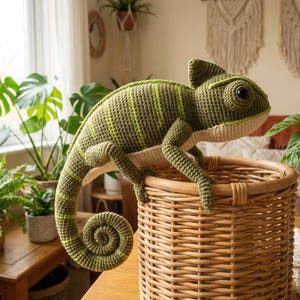 May include: A large, handmade crochet chameleon in shades of green and yellow rests on a woven basket. The reptile features detailed stitching, a curled tail, and realistic eyes. The basket is made of light brown wicker.