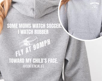 Op de afbeelding: Een grijs gemêleerde hoodie met witte tekst op de achterkant: SOME MOMS WATCH SOCCER. I WATCH RUBBER FLY AT 90MPH TOWARD MY CHILD'S FACE. #GOALIEMOMLIFE. De voorkant toont een kleine witte GOALIE MOM afbeelding op de borst.