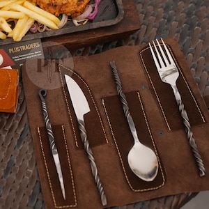 May include: A brown leather cutlery roll containing a metal fork, spoon, and knife with twisted handles, alongside a matching leather case. A business card with the text PLUSTRADERS is visible near a serving tray of cooked meat and vegetables.