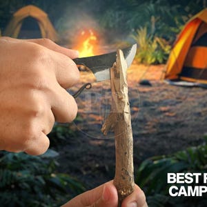 May include: A black camping knife is used to carve a wooden stick. The knife has a curved handle and a sharp blade. The text "BEST FOR CAMPING" is visible in the lower right corner. The background includes tents and a campfire.