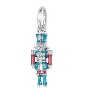 May include: A silver charm depicting a toy soldier nutcracker. The charm is painted in teal, red, and white enamel, with clear crystal accents. The soldier has a star on his hat and a loop for attaching to a bracelet or necklace.