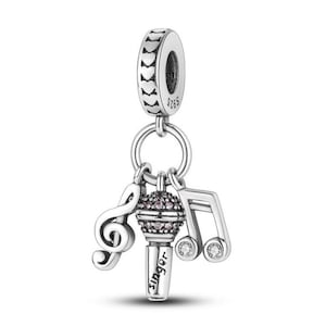 Op de afbeelding: Een zilveren bedel met een muzikaal thema. Het heeft een microfoon met het woord "singer", een G-sleutel en een muzieknoot. De microfoon heeft roze accenten. De bedel is ontworpen om aan een armband of ketting te worden bevestigd.
