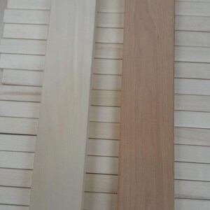 May include: Two rectangular wooden planks, one light beige labelled "Aspen Wood" and the other light brown labelled "Alder wood". The planks are displayed against a background of similar wooden slats.