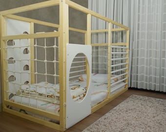 May include: A wooden playpen with a white net and a white door with a round opening. The playpen has a white mattress and a white blanket inside.
