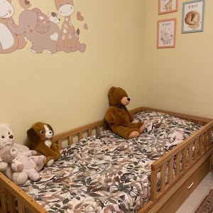 May include: A child's bedroom with a wooden bed, floral bedding, and soft toys. The walls are adorned with animal decals and framed prints with motivational phrases, creating a playful and comforting environment.