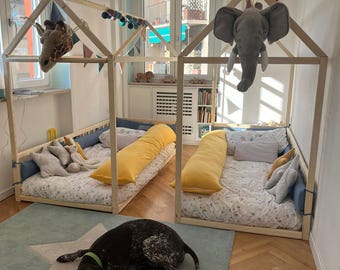 Könnte beinhalten: Zwei Holzbetten mit Stofftierköpfen, einer Giraffe und einem Elefanten, sind zu sehen. Die Betten haben gemusterte Bettwäsche und gelbe Kissen. Ein Hund ruht auf einem blauen Teppich mit einem weißen Stern.