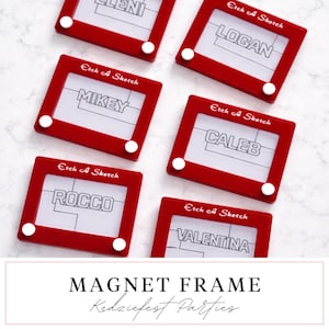 以下が含まれることがあります： 赤いEtch-A-Sketchのおもちゃに似たマグネットフレームが複数あり、それぞれに白い文字で名前が書かれています。名前はELENI、LOGAN、MIKEY、CALEB、ROCCO、VALENTINAです。各フレームには「Etch A Sketch」の文字が印刷されています。画像の下部には「MAGNET FRAME」と書かれています。