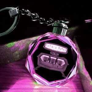 May include: A purple crystal keychain featuring a 3D laser engraved image of a "Pack-A-Punch" machine from the Call of Duty video game series.