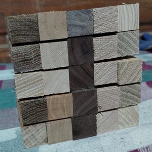 May include: A stack of wooden blocks in various shades of brown and tan. The blocks are square and appear to be made of different types of wood, showcasing varied grain patterns and textures. The arrangement suggests a potential craft or construction project.