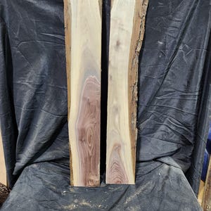May include: Two unfinished wood slabs with natural edges. The wood grain features a mix of light tan, cream, and reddish-brown hues. The slabs are rectangular and appear ready for woodworking projects.