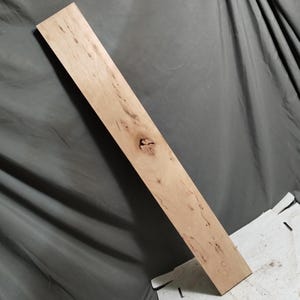 May include: A light-colored, rectangular wooden board with a knot in the center. The wood grain is visible, and the board has a natural, unfinished appearance. The board is approximately 48 inches long.