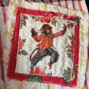 May include: A fabric patch featuring a dancing monkey in a red and orange jacket and dark pants. The monkey is on a white background with floral accents, framed by red fabric and a striped pattern.