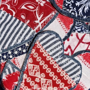 May include: Close-up of several heart-shaped fabric patches in red, white, and blue. The patches feature various patterns, including stripes, floral designs, and stars. Each heart is outlined with a denim-like fabric.