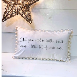 May include: A white rectangular pillow with a pom-pom trim and the text "All you need is faith, trust, and a little bit of pixie dust." A decorative star made of woven twigs hangs above the pillow.