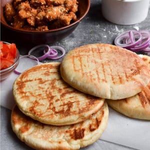 Puede incluir: Primer plano de una comida con panes planos a la parrilla con una superficie marrón y estampada. La imagen también incluye un cuenco de comida frita, aros de cebolla roja y un cuenco pequeño de tomates cortados.