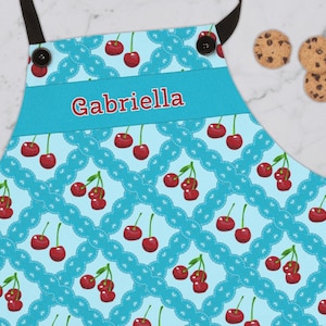 May include: A blue and white apron with a cherry pattern and a personalized name, "Gabriella", on the front.