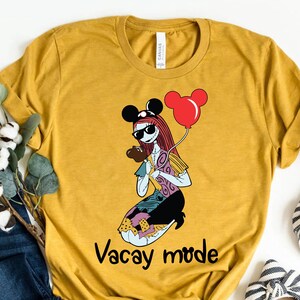 Puede incluir: Una camiseta amarilla mostaza con un gr&aacute;fico de un personaje de dibujos animados con gafas de sol y un sombrero de Mickey Mouse sosteniendo un globo rojo. El texto "Vacay mode" est&aacute; impreso debajo del gr&aacute;fico.
