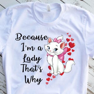 May include: White t-shirt with a black graphic of a white cat with pink bow and the text "Because I'm a lady That's Why" surrounded by pink hearts.