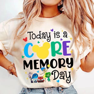 May include: Cream-coloured t-shirt with the text "Today is a CORE MEMORY Day" in black, blue, green, yellow, and purple. The design includes cartoon characters and Mickey Mouse silhouettes. A fun, colourful graphic tee.