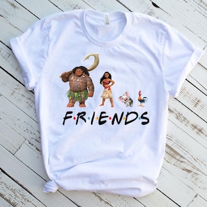 K&ouml;nnte beinhalten: Wei&szlig;es T-Shirt mit einem Grafikdruck von Figuren aus dem Animationsfilm Vaiana. Die Figuren sind Maui, Vaiana, Pua das Schwein und Hei Hei der Hahn. Der Text "FRIENDS" ist unter den Figuren gedruckt.
