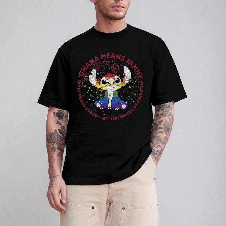 May include: Black t-shirt with a colourful graphic of the character Stitch from Lilo & Stitch. The design includes the text "OHANA MEANS FAMILY" in a circular arrangement around the character. The shirt has a crew neck and short sleeves.