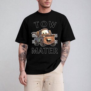 May include: Black t-shirt featuring a cartoon image of Tow Mater from the movie Cars. The text "TOW MATER" is printed above and below the character in white block letters. The design includes a checkered flag pattern.