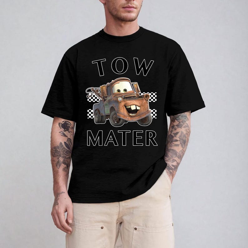 May include: Black t-shirt featuring a cartoon image of Tow Mater from the movie Cars. The text "TOW MATER" is printed above and below the character in white block letters. The design includes a checkered flag pattern.