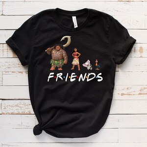 K&ouml;nnte beinhalten: Schwarzes T-Shirt mit einem Aufdruck von Figuren aus dem Film Vaiana. Die Figuren sind Maui, Vaiana, Pua das Schwein und Hei Hei der Hahn. Der Text "FRIENDS" ist unter den Figuren aufgedruckt.